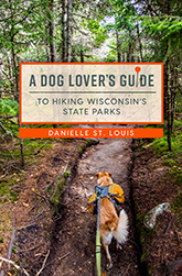 A Dog Lover's Guide: cover showing Lucky the Labrador-border collie walking up a steep, muddy path lined with coniferous trees. The title text is written in green font within an orange box.